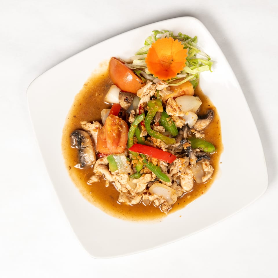 Stir-fried chicken with mushrooms, onions, tomatoes, and peppers in brown sauce, garnished with lettuce and carved carrot.