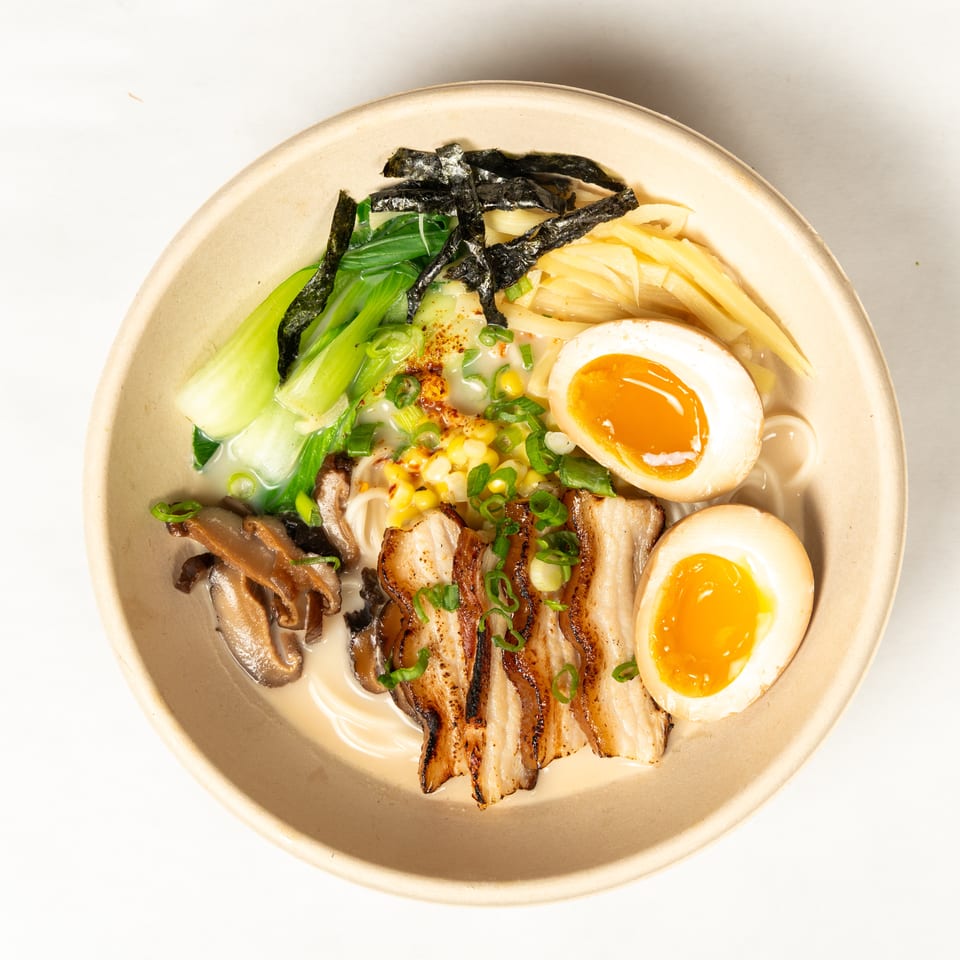 Overhead bowl of ramen with sliced pork, soft-boiled eggs, mushrooms, bok choy, corn, scallions, and seaweed.